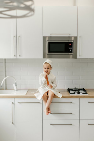 A girl in a white coat sits on the kitchen table and eats marmalade.の写真素材