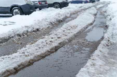 The road is covered with snow and slush, cars are parked on the side of the road. winter city.の写真素材