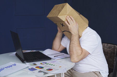 A man is a businessman in a white shirt with a paper bag on his head, with a drawn sad emoticon,...