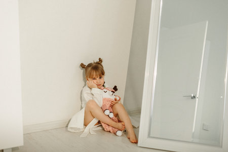 A girl in a bathrobe plays on the floor with a knitted unicorn.の写真素材