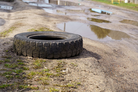 a black car tire lies on the side of an old dirt road with pits and puddles.の写真素材