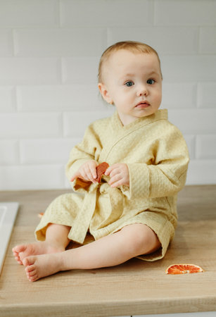 A girl in a yellow bathrobe sits on the kitchen table and eats marmalade.の写真素材