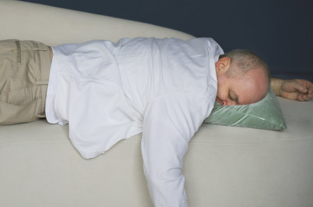 An exhausted overworked man in a casual shirt came home after work and plopped down on the couch feeling tired.の写真素材