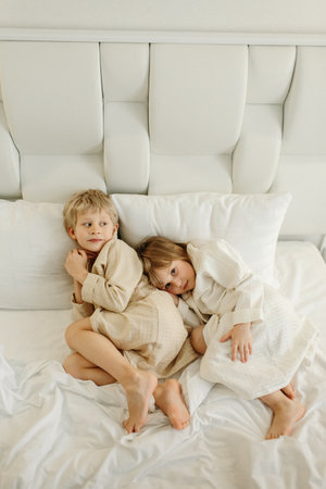 Brother and sister lying on the bed in bathrobes after a shower.の写真素材