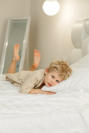 Portrait of a boy in a bathrobe, who lies on the bed and looks at the camera. vertical frame.の写真素材
