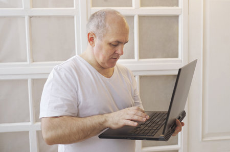 A man holds a laptop in his hands, stands at home and communicates in social networks, writes a message.の写真素材