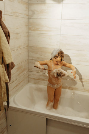 A preschool girl is washing herself with a big brush in the bathroom.の写真素材