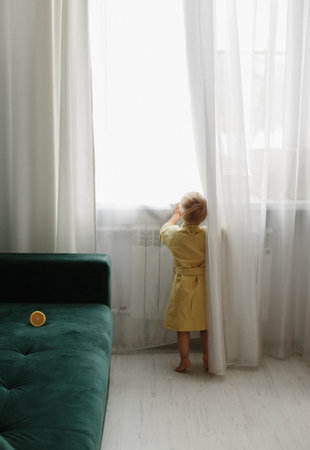 A little boy in a dressing gown stands near the window and looks.の写真素材