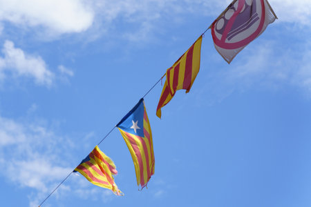 The flags of Catalonia hang on a cable, developing in the wind against the blue sky in the rays of the sun.の写真素材