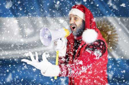 Santa Claus shouts into a bullhorn and shows an aggressive gesture with his hand against the background of the flag of Argentina.の写真素材