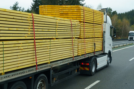 A truck transports lumber - boards on a motorway on a semi-trailer. In the background forest and mountains. logistics concept.の写真素材