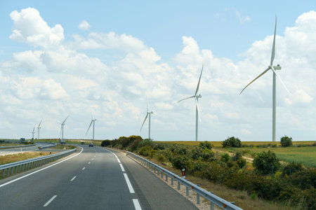 Wind turbines stand along the road against the background of clouds. Production of green ecological energy.の写真素材