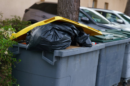 A gray trash can filled with trash, topped with a yellow lid.の写真素材