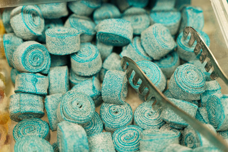 There are candies on the counter - blue chewing marmalade on a roll and tongs. Candy store.の写真素材
