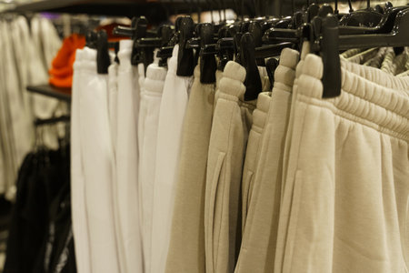 Women's beige and white trousers hang on hangers in a clothing store. Close-up, background....
