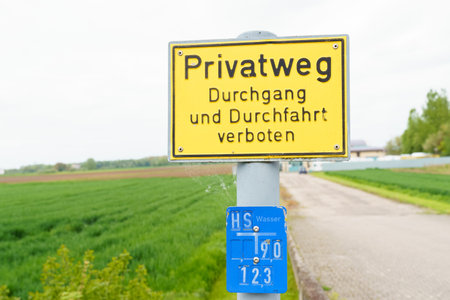 There is a yellow sign by the road with the inscription - Access to and travel on the private road is prohibited. The inscription on the sign is in German.の写真素材