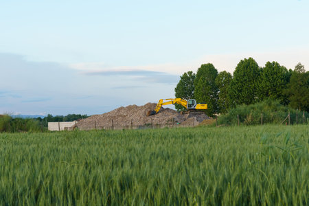 A hydraulic excavator on a pile of crushed construction waste against the backdrop of a green field. Construction concept.の写真素材