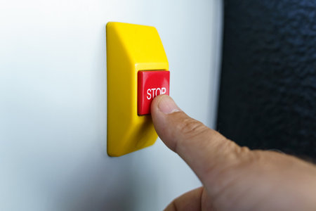 Stop button and the hand of a worker about to press it. Emergency stop button, close-up.の写真素材