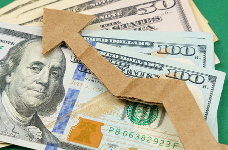 Dollars and a cardboard arrow pointing up lie on a green surface. Economic growth.