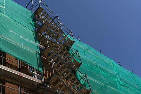 Scaffolding for renovation of building facades, covered with protective green mesh. Building...