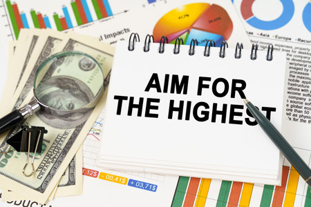 Business concept. On the table are business charts, dollars and a notepad with the inscription - AIM FOR THE HIGHESTの写真素材