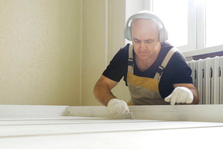 Furniture assembly. A worker fastens the parts of a bed using a confirmat. While working, he listens...