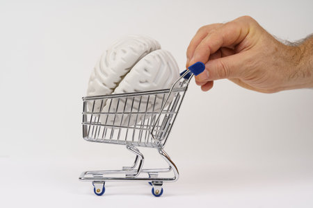 Against a white background, a close-up of a hand rolling out a shopping cart with a human brain...