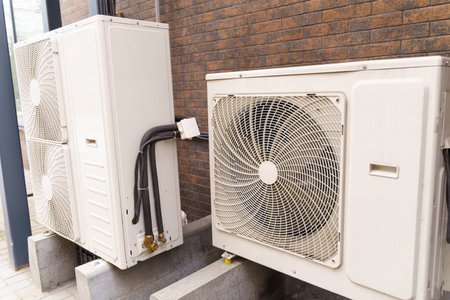 A white air conditioner unit positioned next to a weathered brick wall on a sunny day.の写真素材