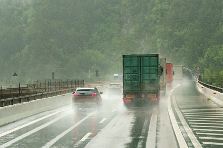 Trucks and cars move forward along the wet highway, their taillights glowing through the heavy downpour and the greenery on their sides blurred.の写真素材