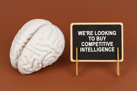On a brown background, a model of the brain and a sign with the inscription - We're looking to buy competitive intelligence. Business and technology concept.の写真素材