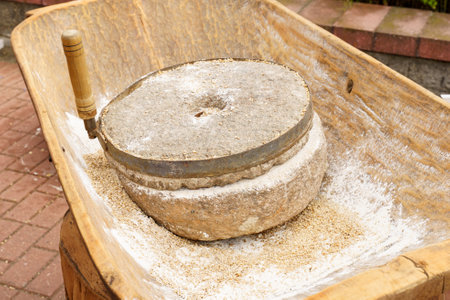 A close-up of an old-fashioned stone mill used for grinding grains, positioned on a wooden table...