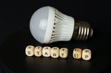 A light bulb lies next to wooden letter blocks spelling out START UP, symbolizing the beginning of a...