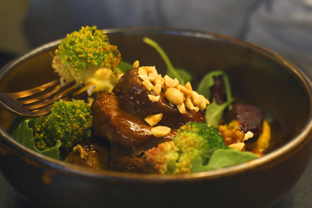 This gourmet dish of roasted meats and glazed vegetables and nuts, served in a stylish dark bowl, is ready for a healthy dinner.の写真素材