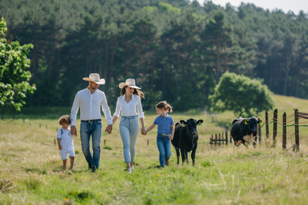 A man, woman, and child are walking in a field with cows grazing around them.の素材