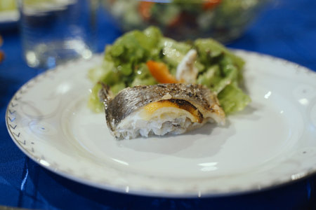A carefully prepared fish dish, complemented by a fresh salad, is presented on a white plate with a...