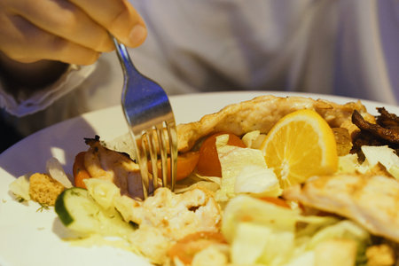 A person sitting at a table cutting into a plate of food using a knife and fork.の写真素材
