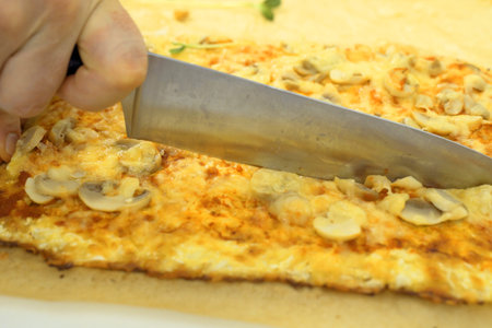 A person is seen cutting a piece of pizza with a knife on a wooden cutting board.の写真素材