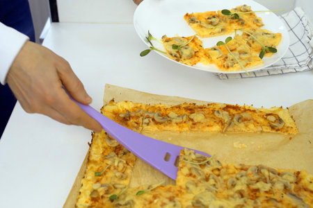A person is seen cutting a slice of pizza using a purple spatula.の写真素材