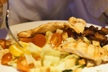 A person sitting at a table cutting into a plate of food using a knife and fork.の写真素材