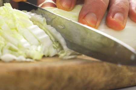 A person is shown cutting up a cabbage on a wooden cutting board with a sharp knife.の写真素材