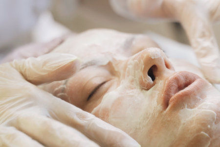 A woman lying down with eyes closed as a therapist massages her face using gentle and soothing...