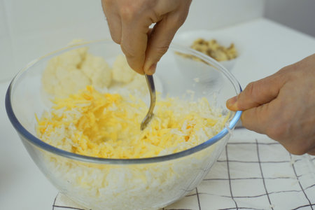 Preparing vegetarian pizza, a man mixes gratified cheese, cauliflower and eggs in a glass bowl.の写真素材
