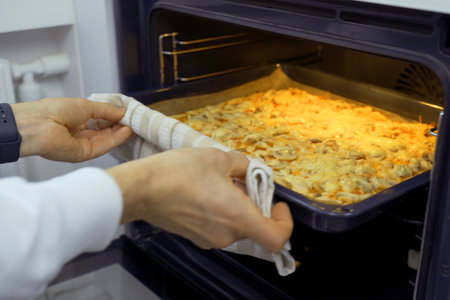 A man wearing oven mitts pulls a tray of freshly baked vegetarian pizza out of a hot oven as steam rises.の写真素材