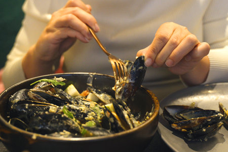 A person is seen eating a bowl of mussels using a fork.の写真素材