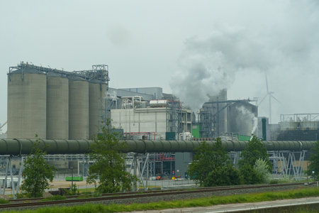 A factory releasing billowing smoke from its tall stacks into the sky, indicating active industrial processes and pollution.の写真素材