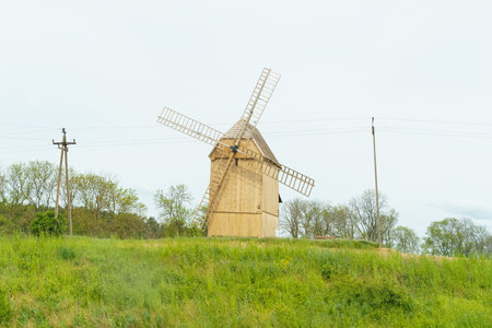 A windmill stands tall on a vibrant green hillside, surrounded by lush vegetation under a clear sky.の写真素材
