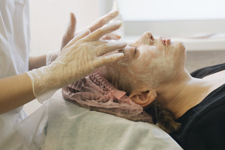 A woman lying down with eyes closed as a therapist massages her face using gentle and soothing motions.の写真素材