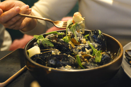 A person is seen eating a bowl of mussels using a fork.の写真素材