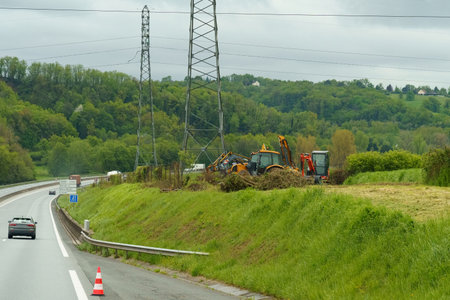 Heavy machinery vehicles are parked on the side of a road, surrounded by grass and trees.