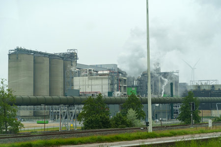 A factory releasing billowing smoke from its tall stacks into the sky, indicating active industrial processes and pollution.の写真素材